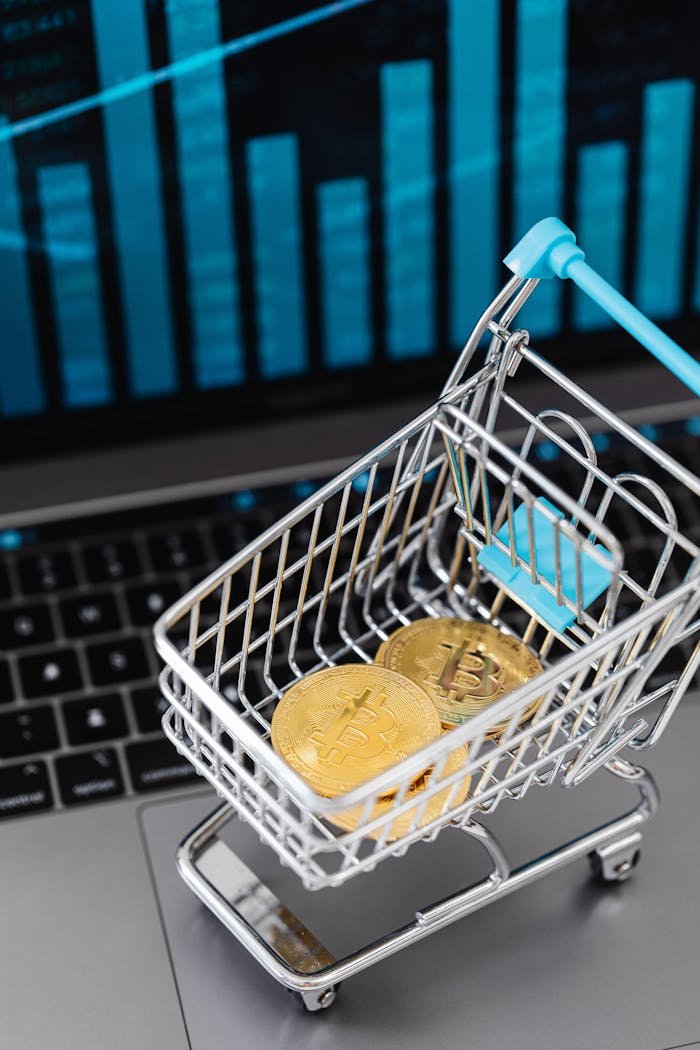 Mini shopping cart with bitcoins and laptop, symbolizing cryptocurrency investment and online trading.